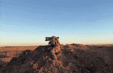 a soldier is sitting on top of a pile of dirt holding a rifle