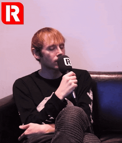 a man sitting on a couch holding a microphone with the letter r above him