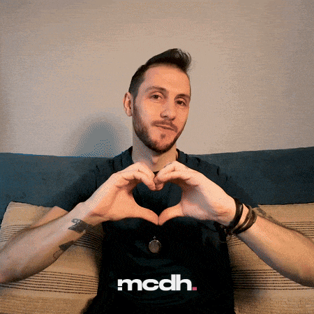 a man sitting on a couch making a heart shape with his hands and the word mcdh behind him