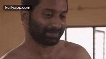 a shirtless man with a beard is standing in front of a window and smiling .