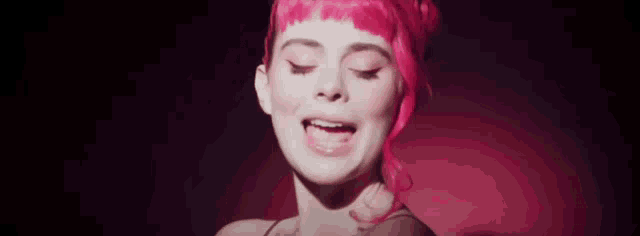 a woman with bright pink hair is singing into a microphone in a dark room .