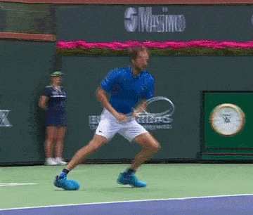 a man in a blue shirt is holding a tennis racquet on a tennis court in front of a wall that says masimo