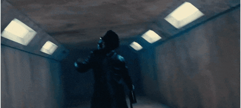 a man in a black coat and hat is walking down a dark tunnel