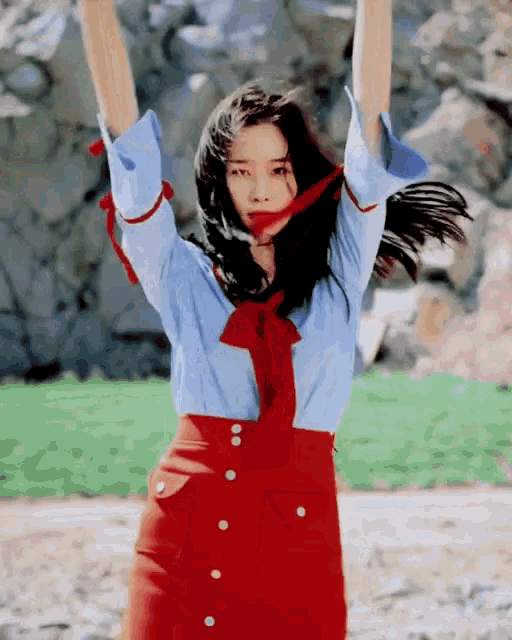 a woman in a blue shirt and red skirt is dancing with her arms up in the air .