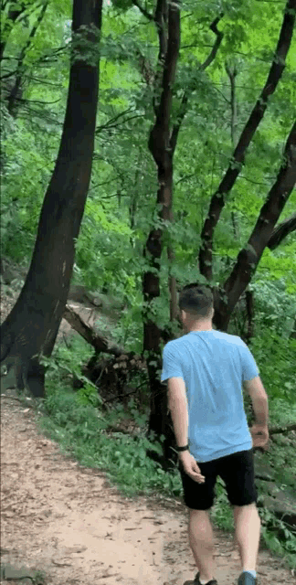 a man in a blue shirt and black shorts is walking down a dirt path in the woods