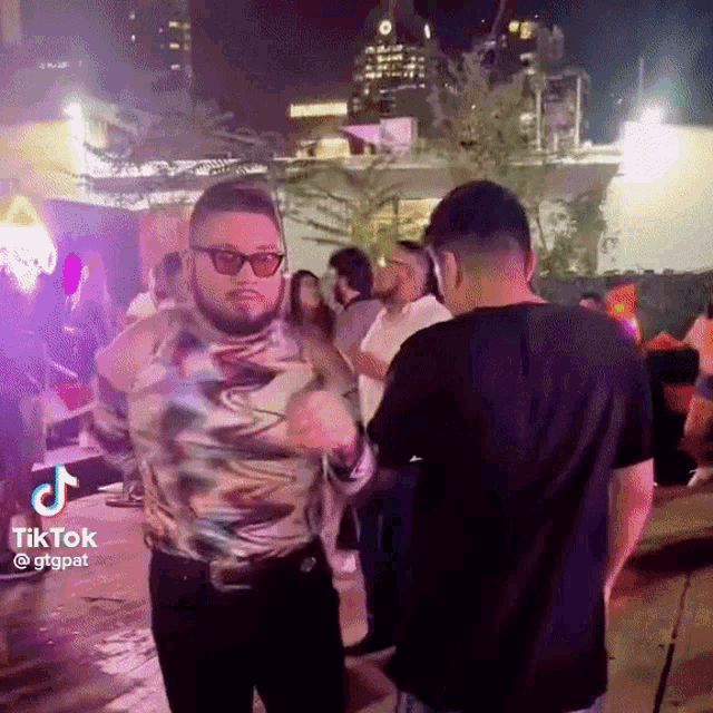 a man wearing sunglasses is dancing in front of a crowd of people .
