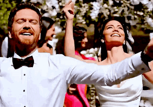 a man in a tuxedo and bow tie stands next to a woman in a wedding dress