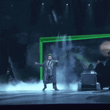 a man in a striped suit is dancing on a stage with a green light behind him