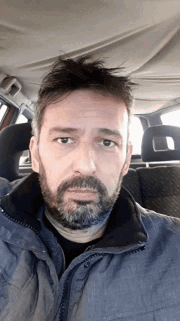 a man with a beard and a jacket is sitting in the back seat of a car