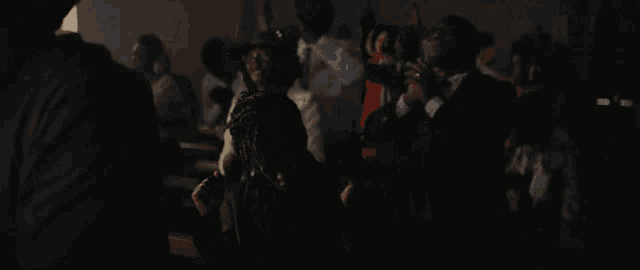 a group of people are gathered in a dark room and one of them is wearing glasses