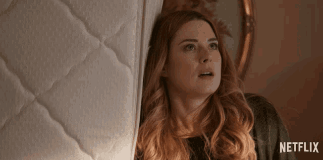 a woman peeking out from behind a mattress with a netflix logo on the bottom
