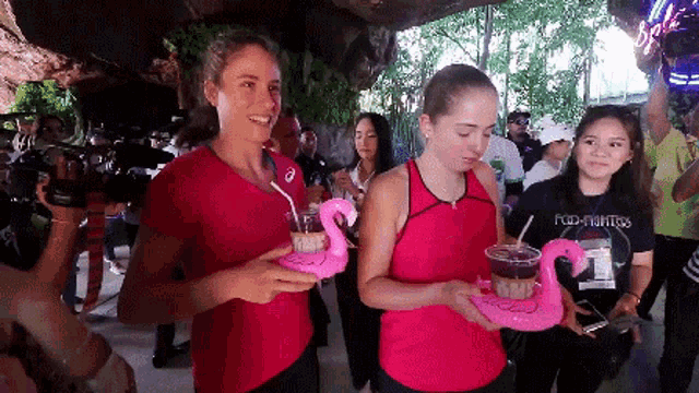 two women in pink tank tops are carrying flamingo floats
