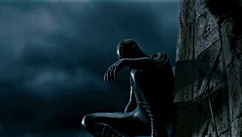 a statue of spider-man is sitting on a rock in the dark .