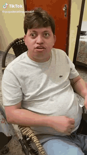 a man in a white shirt with a lacoste logo on it is sitting in a chair ..