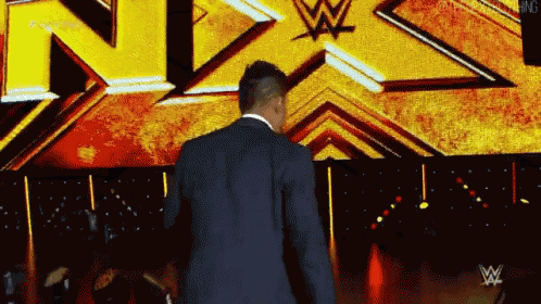 a man in a suit is walking in front of a screen that says nxt on it