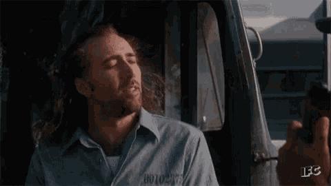 a man with long hair and a beard is smiling while sitting in the driver 's seat of a truck .