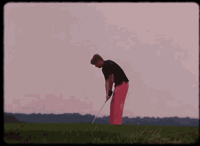 a man in pink pants is swinging a golf club on a green field