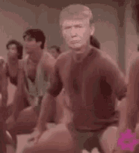 a man in a red shirt is dancing in front of a group of people in a gym .