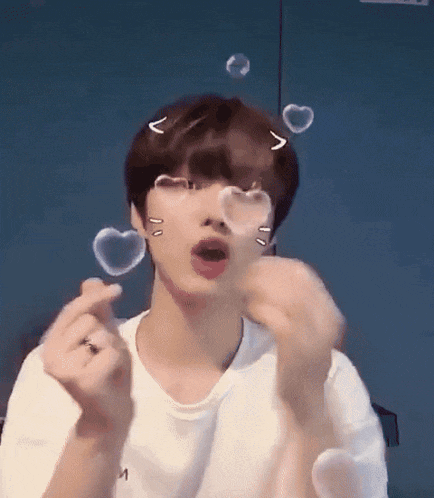 a young man is blowing soap bubbles in the shape of hearts on his face .