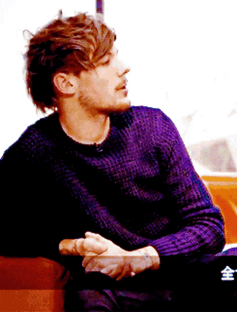 a man wearing a purple sweater is sitting on a couch