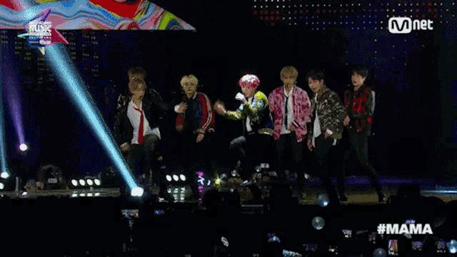 a group of young men are dancing on a stage in front of a mnet banner