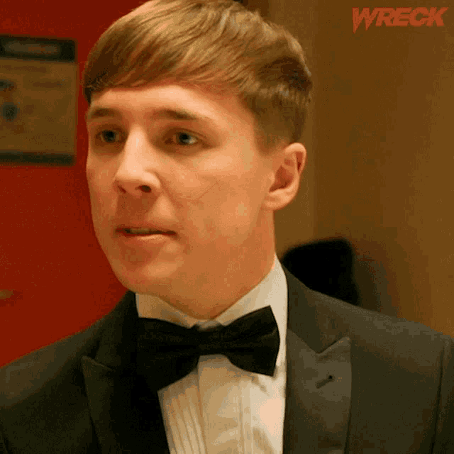 a man in a tuxedo with a bow tie is standing in front of a sign that says wreck