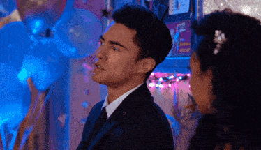 a man in a suit stands next to a woman in a room with balloons