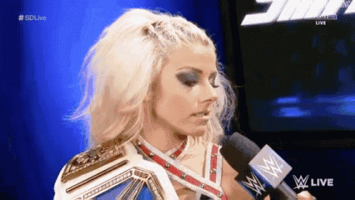 a woman is talking into a microphone while holding a wrestling championship belt .