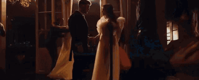 a man in a suit is holding a woman 's hand in a dark room .