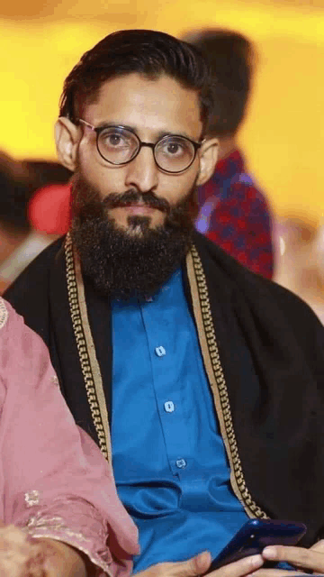 a man with glasses and a beard is wearing a blue shirt and a black shawl