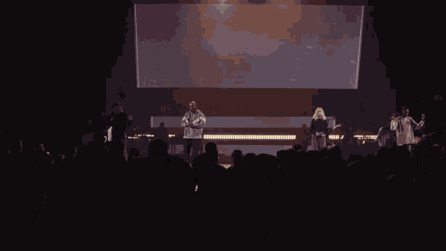 a group of people singing on a stage in front of a large screen