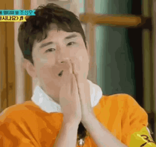 a man in an orange shirt is praying with his hands folded .