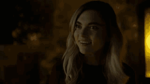 a woman is smiling in a dark room with a yellow light behind her