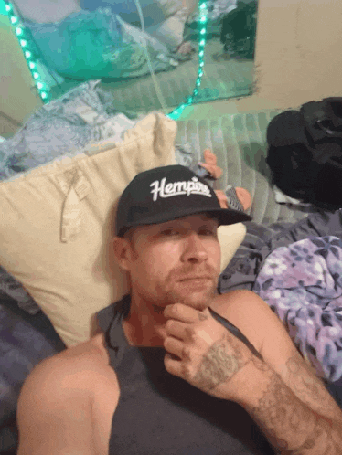 a man laying on a bed wearing a black hat with the word hemp on it