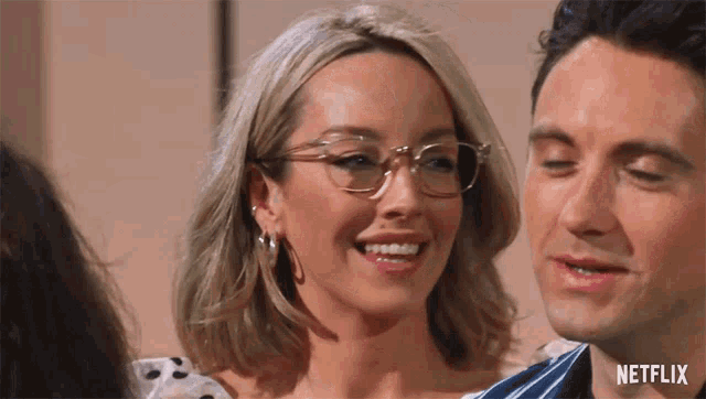 a woman wearing glasses is smiling next to a man with netflix written on the bottom