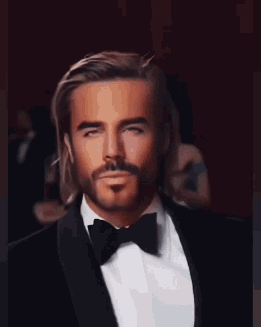a man with long hair and a beard is wearing a tuxedo