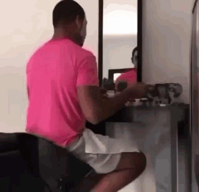 a man in a pink shirt and white shorts is sitting in front of a mirror