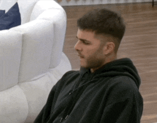 a man wearing a black hoodie is sitting on a couch .