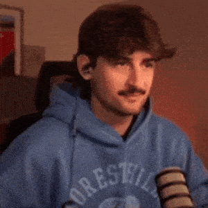 a man in a blue hoodie is sitting in front of a microphone and looking at the camera .