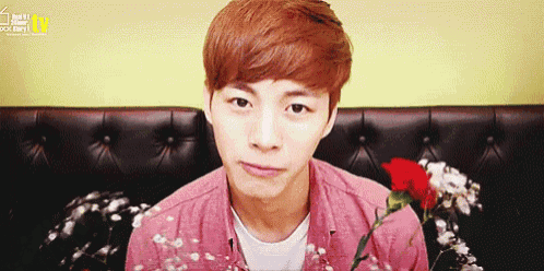 a young man with red hair is sitting on a couch with a red rose in front of him .