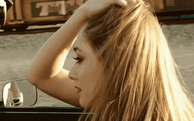 a woman adjusts her hair while looking out the window of a car