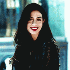 a woman with long black hair and red lipstick is smiling