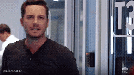 a man in a black shirt is standing in front of a glass door in a room .
