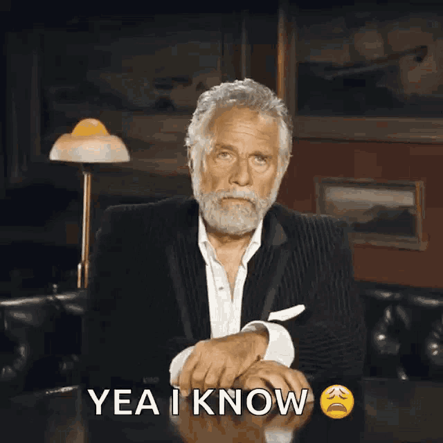a man with a beard is sitting at a table with the words yea i know below him