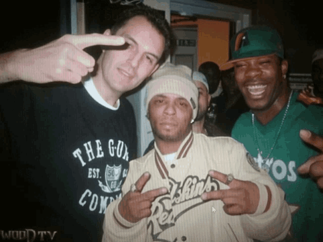 three men posing for a picture with one wearing a shirt that says " the gun "