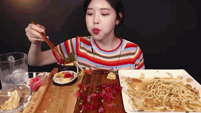 a woman in a striped shirt is eating sushi and spaghetti with chopsticks