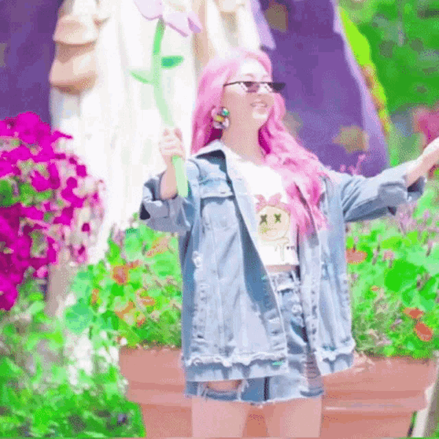 a girl with pink hair is wearing a denim jacket and shorts and is holding a flower .