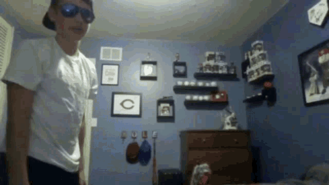 a boy wearing sunglasses and a hat is standing in a room with pictures on the wall