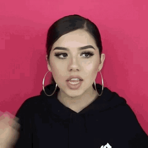 a woman wearing hoop earrings and a hoodie is making a funny face .