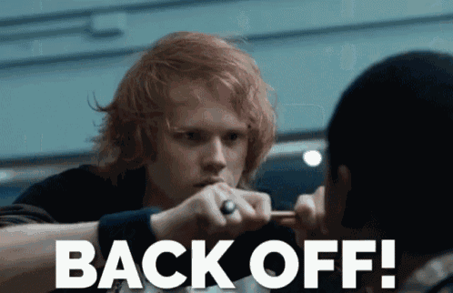 a man with red hair holds a knife in front of another man with the words back off